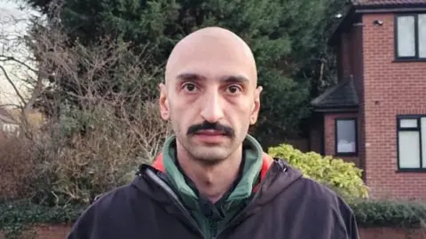 British Iranians take to streets of Manchester hours after US-Israeli strikes handout Farid Vahidi poses on a street with trees behind. He wears as dark coat over a top in the green and red colours of the Iranian flag