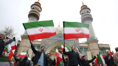 British Iranians take to streets of Manchester hours after US-Israeli strikes EPA A crowd of men wave Iranian flags outside an ornate mosque with two minarets.